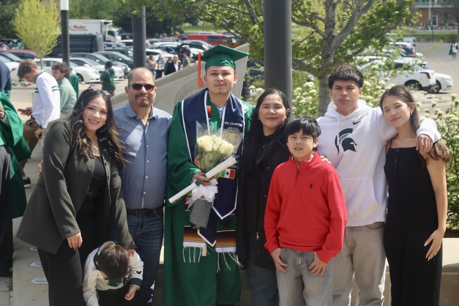 First-generation graduate holding flowers and celebrating commencement with extended family