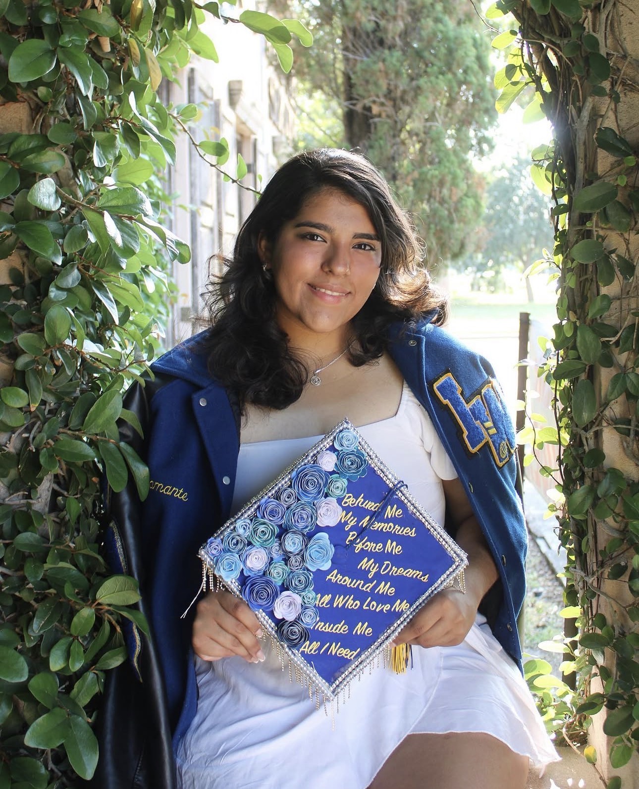 Graduate holding a decorated graduation cap in a garden portrait